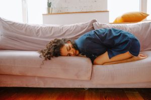 the infradian rhythm, girl lying on couch in fetus pose, cramp, menstruation, linh dang hypnocoach, transformational coach, rtt practitioner, hypnotherapist